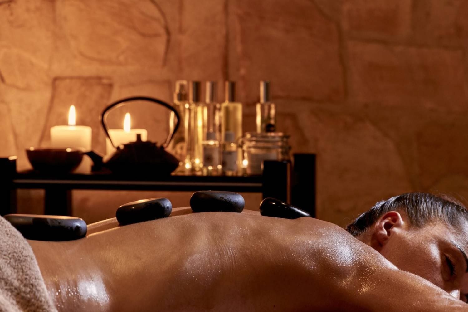 Hot stone massage along a guest's back in a warm, candlelit treatment room at Zoe Spa Mykonos