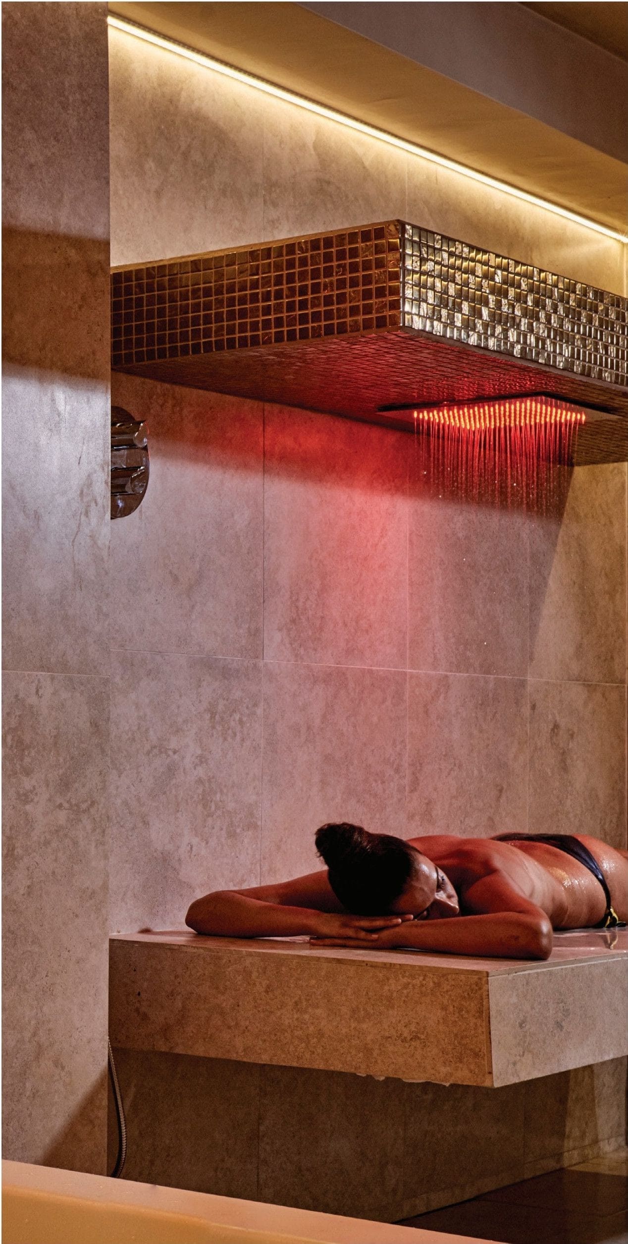 Guest on a stone table under a red chromatherapy rainfall shower in the wet area at Zoe Spa Mykonos